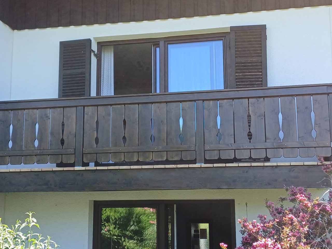 Dunkel lasierter Holzbalkon mit gefrästen Geländerstäben an einem weiß verputzten Wohnhaus