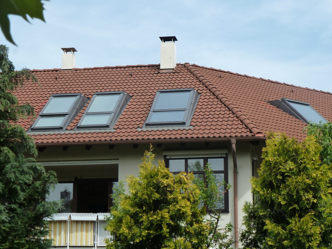 Wohnhaus mit rotem Ziegel-Walmdach, mehrere Dachflächenfenster in Reihe, zwei verputzte Schornsteine