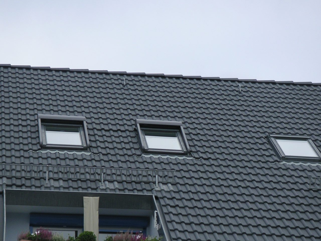 Anthrazitfarbenes Ziegeldach mit drei Dachflächenfenstern und einer Dachloggia