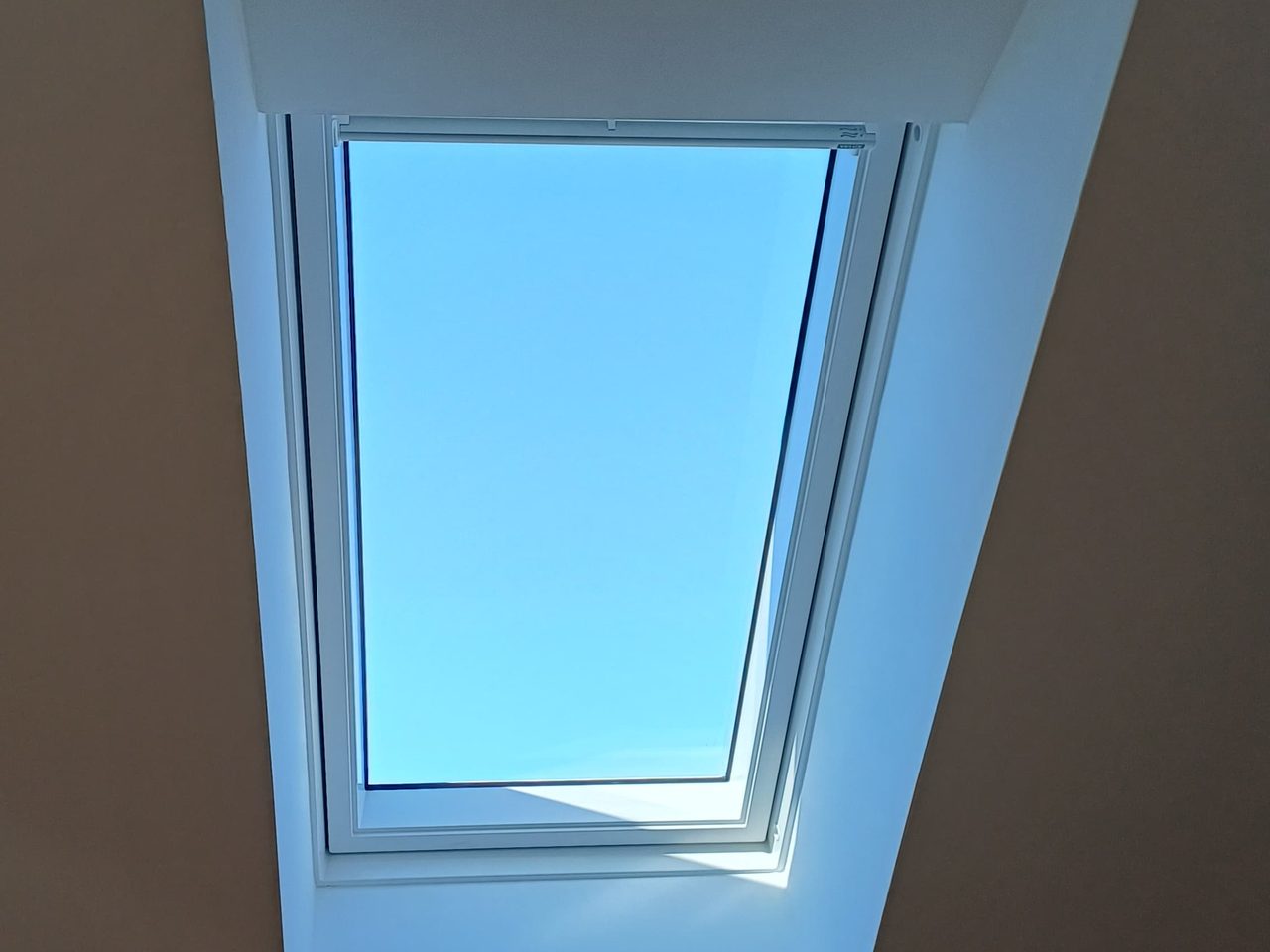 Dachflächenfenster von innen gesehen, glatt verputzte weiße Laibung, blauer Himmel