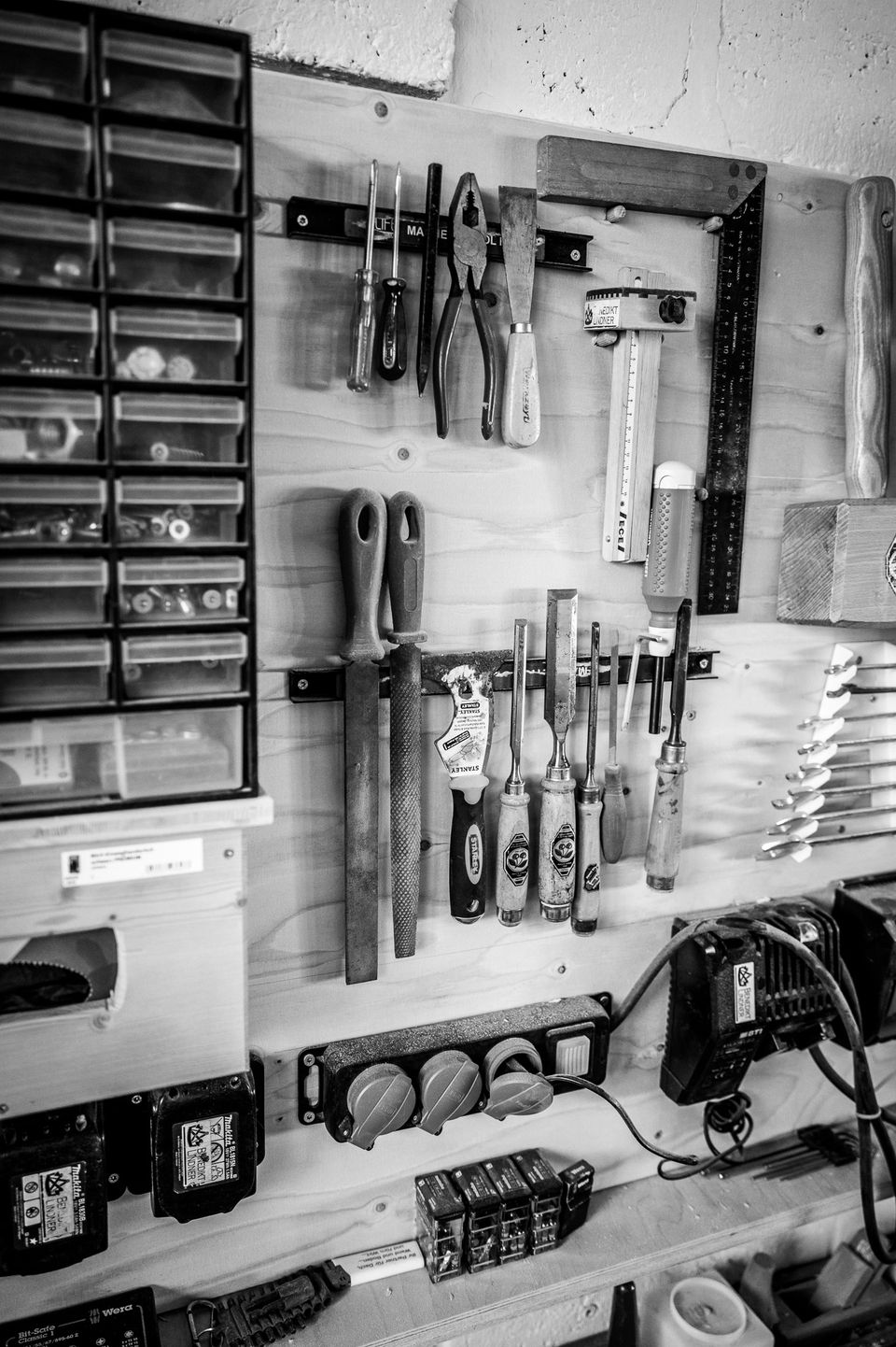Werkzeugwand in unserer Werkstatt: Stechbeitel, Feilen, Zangen und ein Winkel an Magnetleisten, darunter Akkus und Ladegeräte